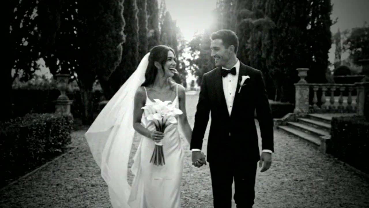 A bride and groom walking hand in hand down a cypress-lined garden path