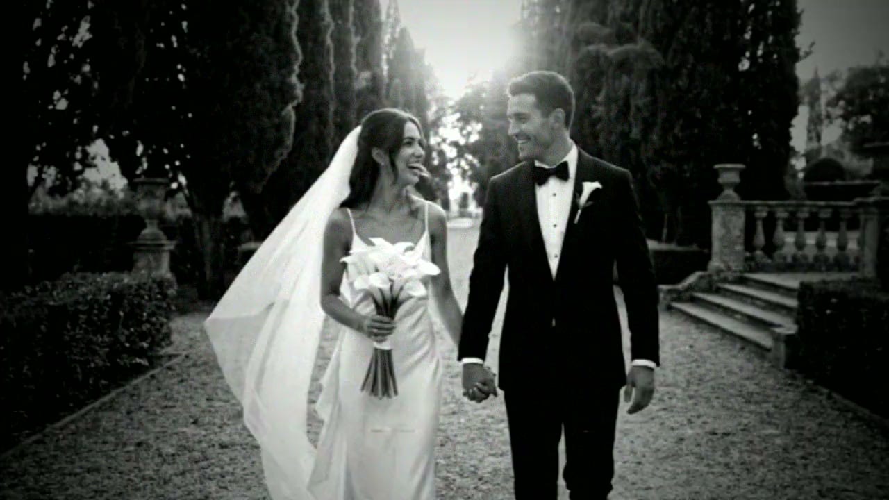 A bride and groom walking hand in hand down a cypress-lined garden path